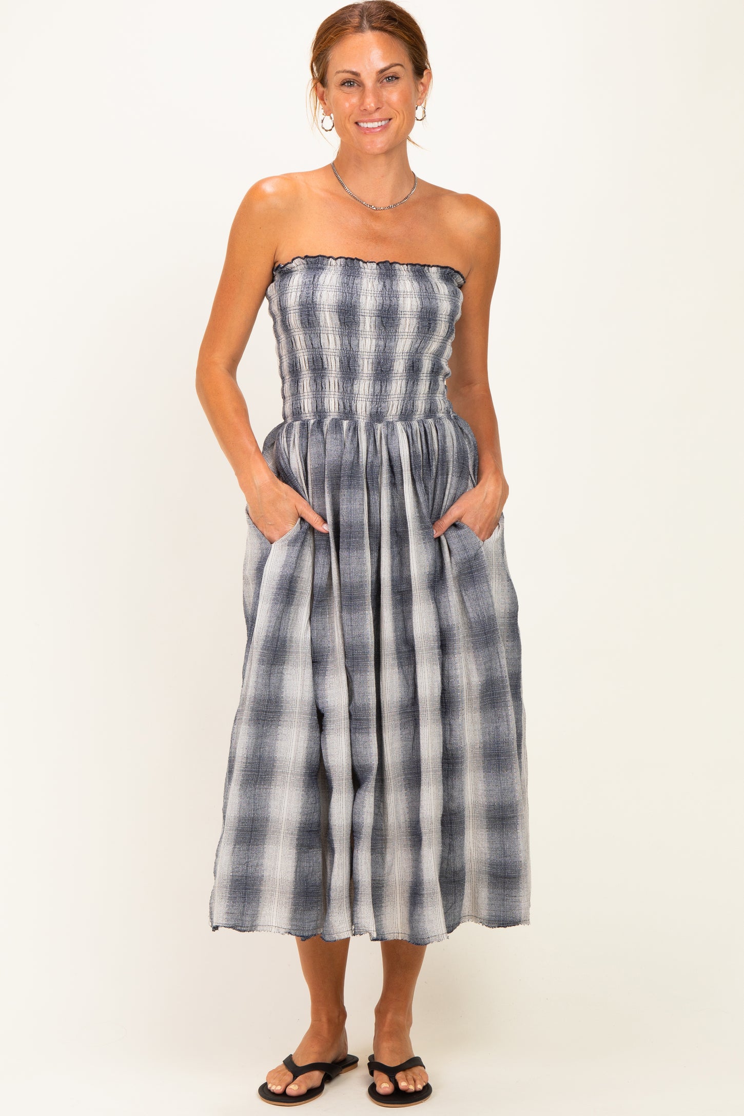 woman wearing a strapless midi dress with a gray and white plaid pattern and side pockets