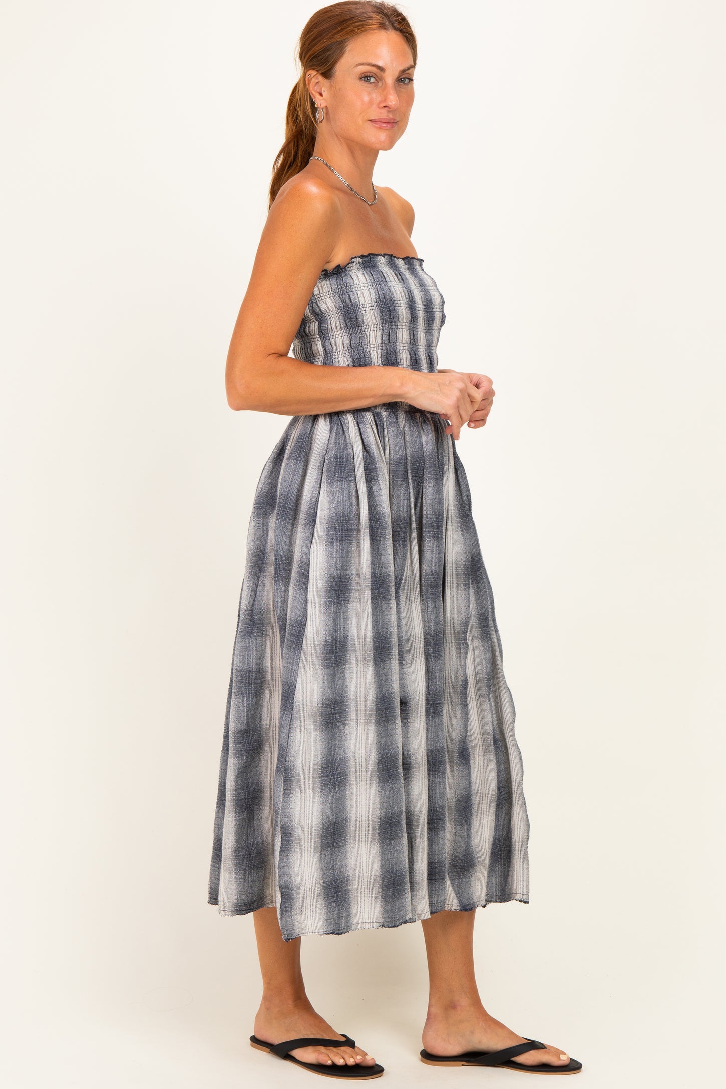 woman wearing a strapless gray and white plaid midi dress with smocked bodice and flowy skirt