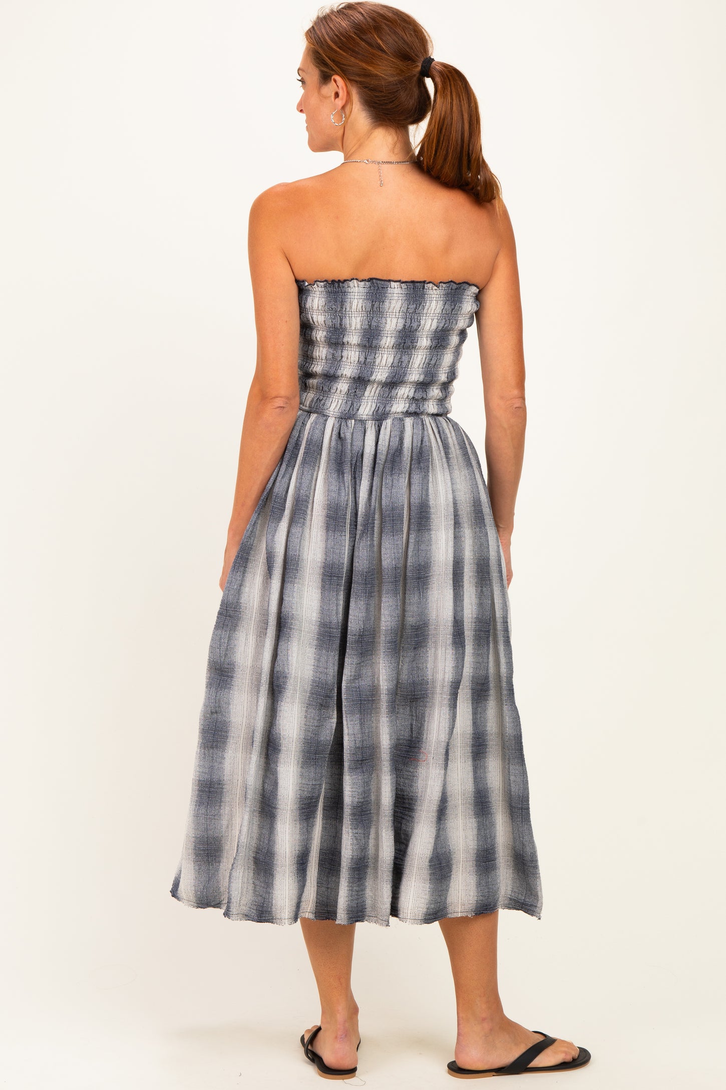 woman wearing a strapless midi dress with a smocked bodice and blue and white plaid pattern, seen from the back