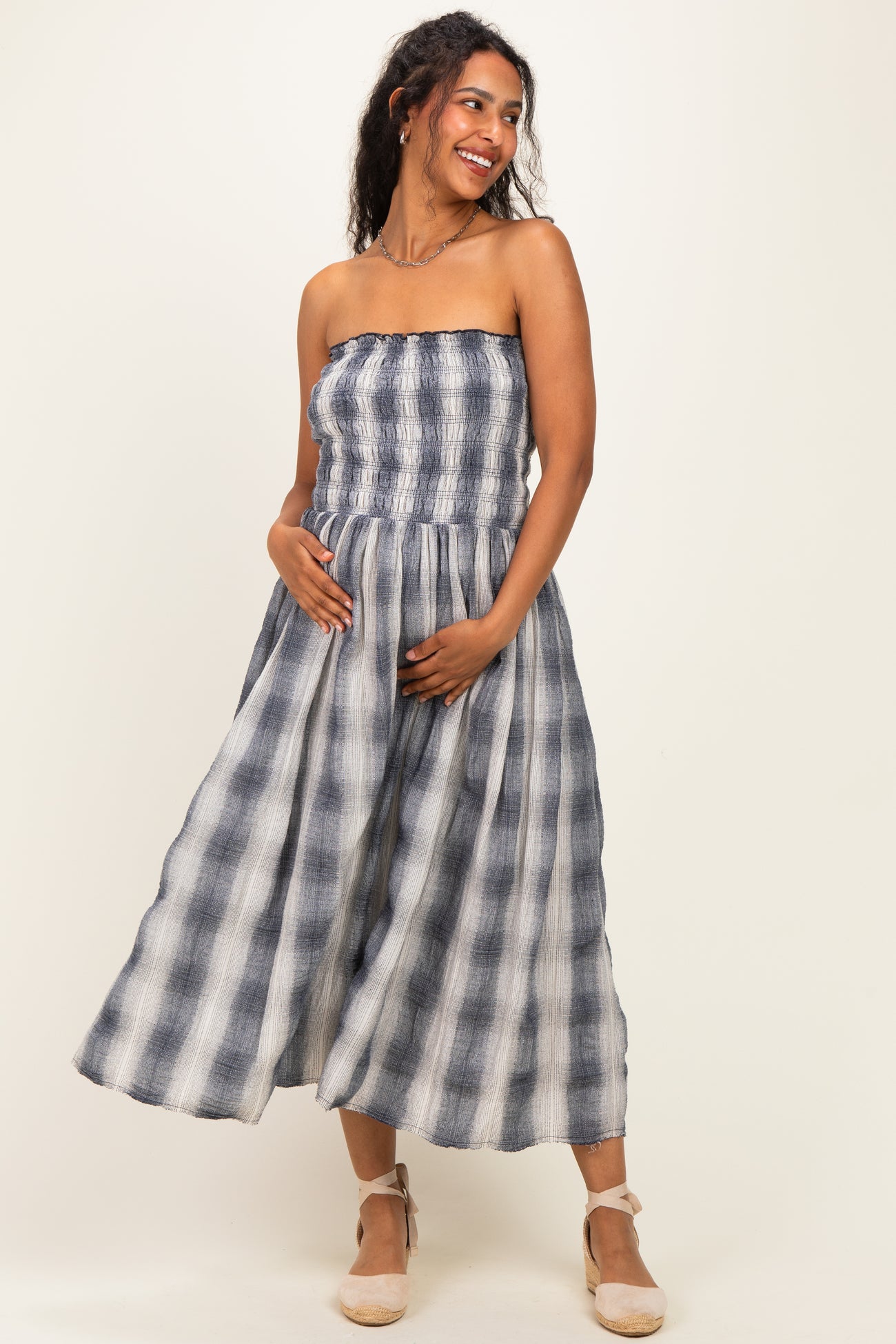 woman wearing a navy and white striped maternity maxi dress with a smocked bodice and holding her baby bump
