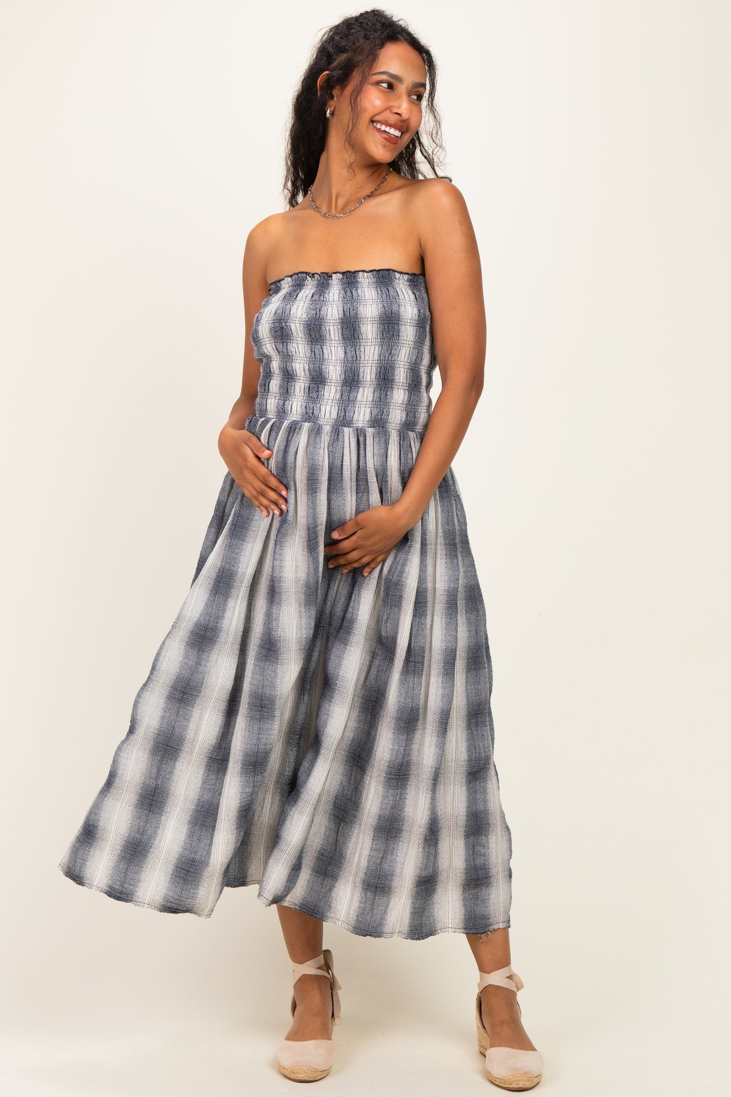 woman wearing a navy and white striped maternity maxi dress with a smocked bodice and holding her baby bump