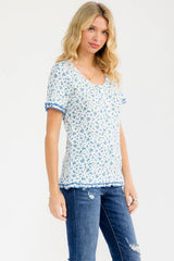 woman wearing a floral print short sleeve top with blue trim and distressed jeans