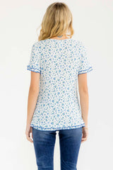 woman wearing a white short sleeve top with blue floral print and ruffle details, view from the back