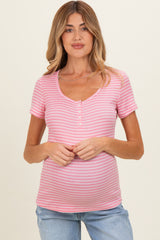 woman wearing a light pink striped maternity top with a v-neck and button detail, holding her baby bump