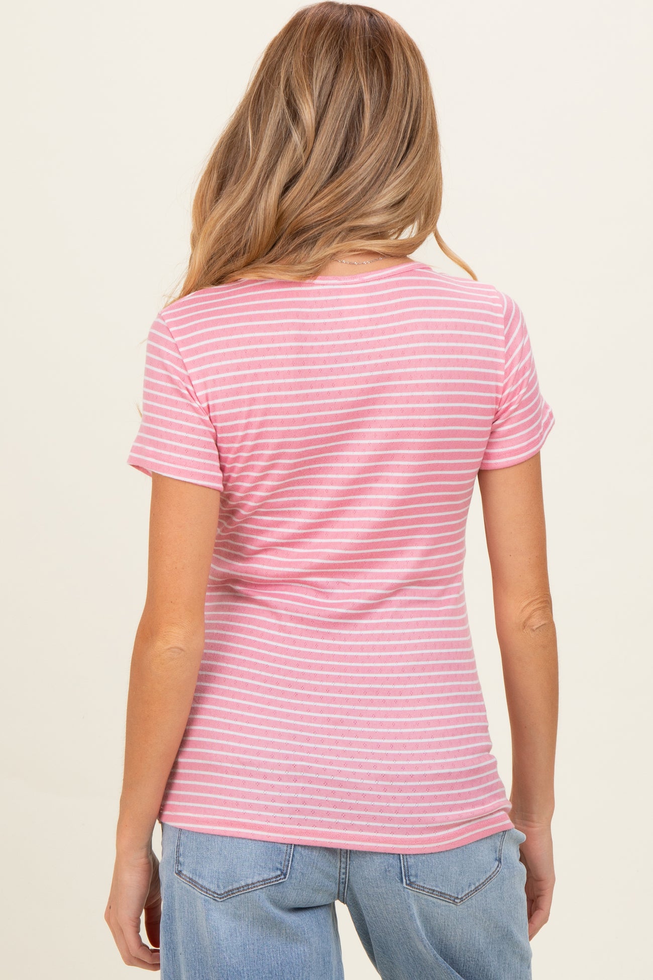 woman wearing a pink striped maternity top, viewed from the back, paired with light blue jeans