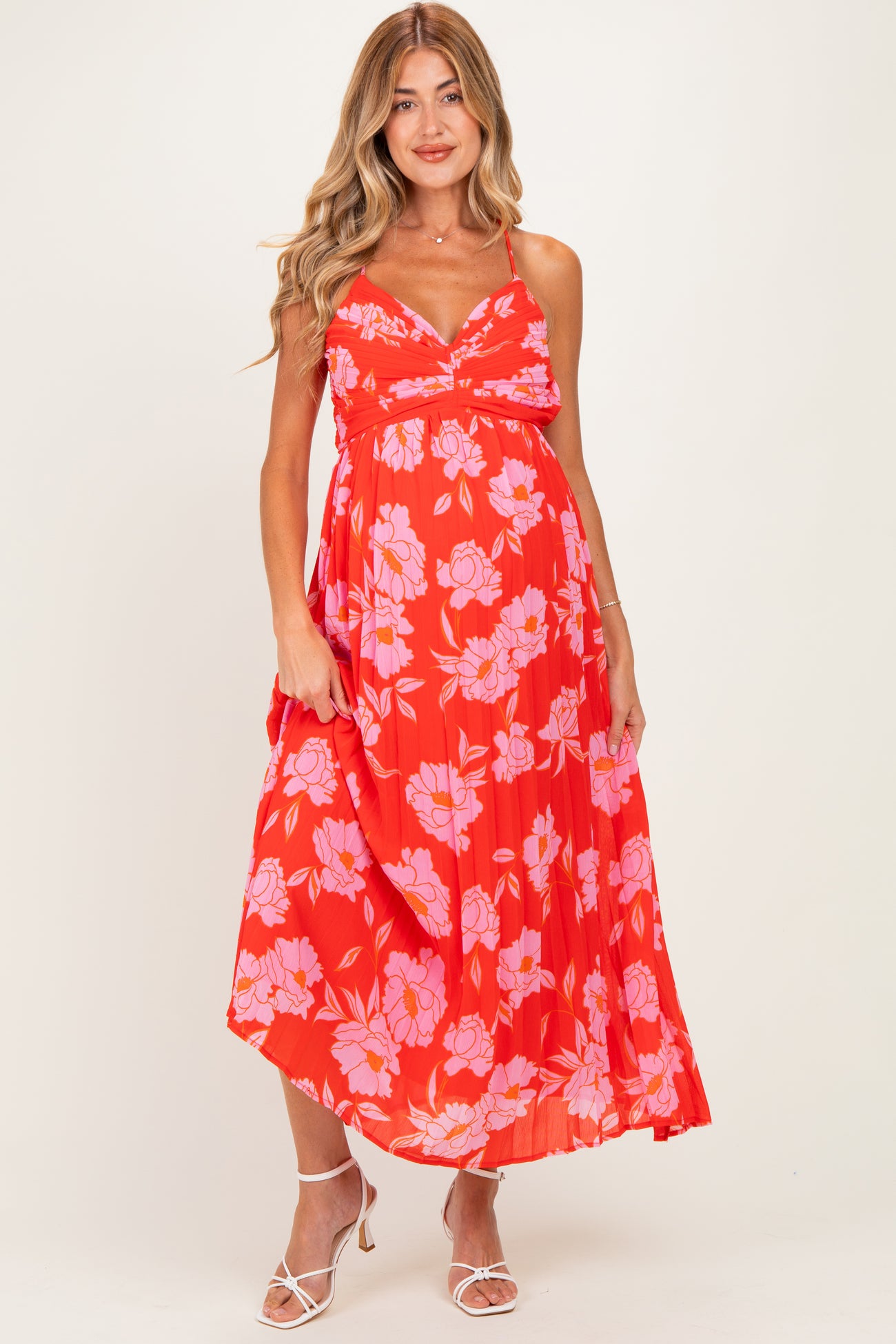 woman wearing a red floral maternity dress with an empire waist and flowy skirt, showcasing her baby bump