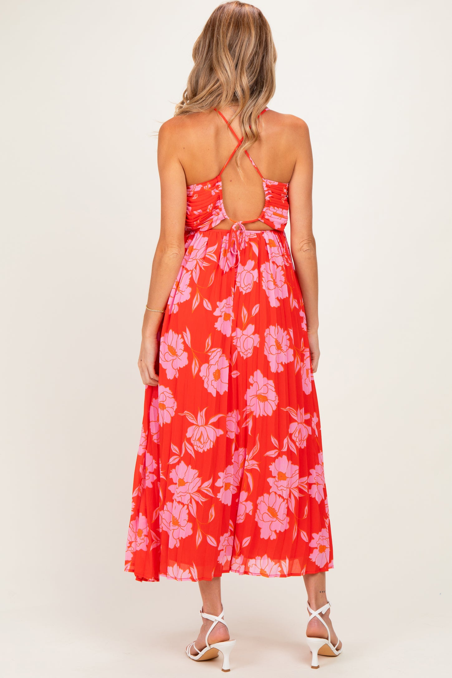 woman wearing a red floral midi maternity dress with a tie back and pleated skirt, showing a baby bump