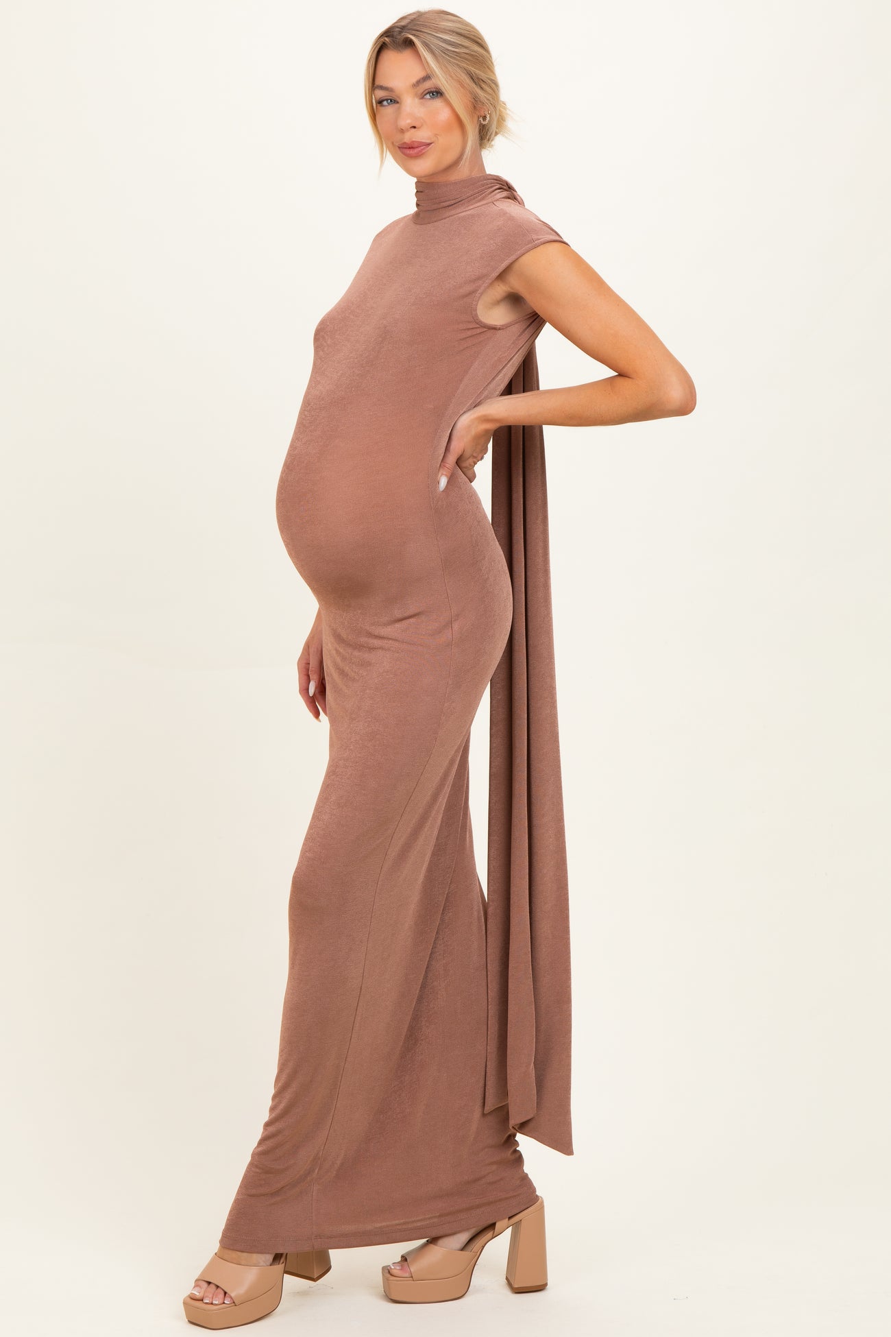 woman wearing a brown maternity maxi dress with a high neckline and draped fabric, showing her baby bump