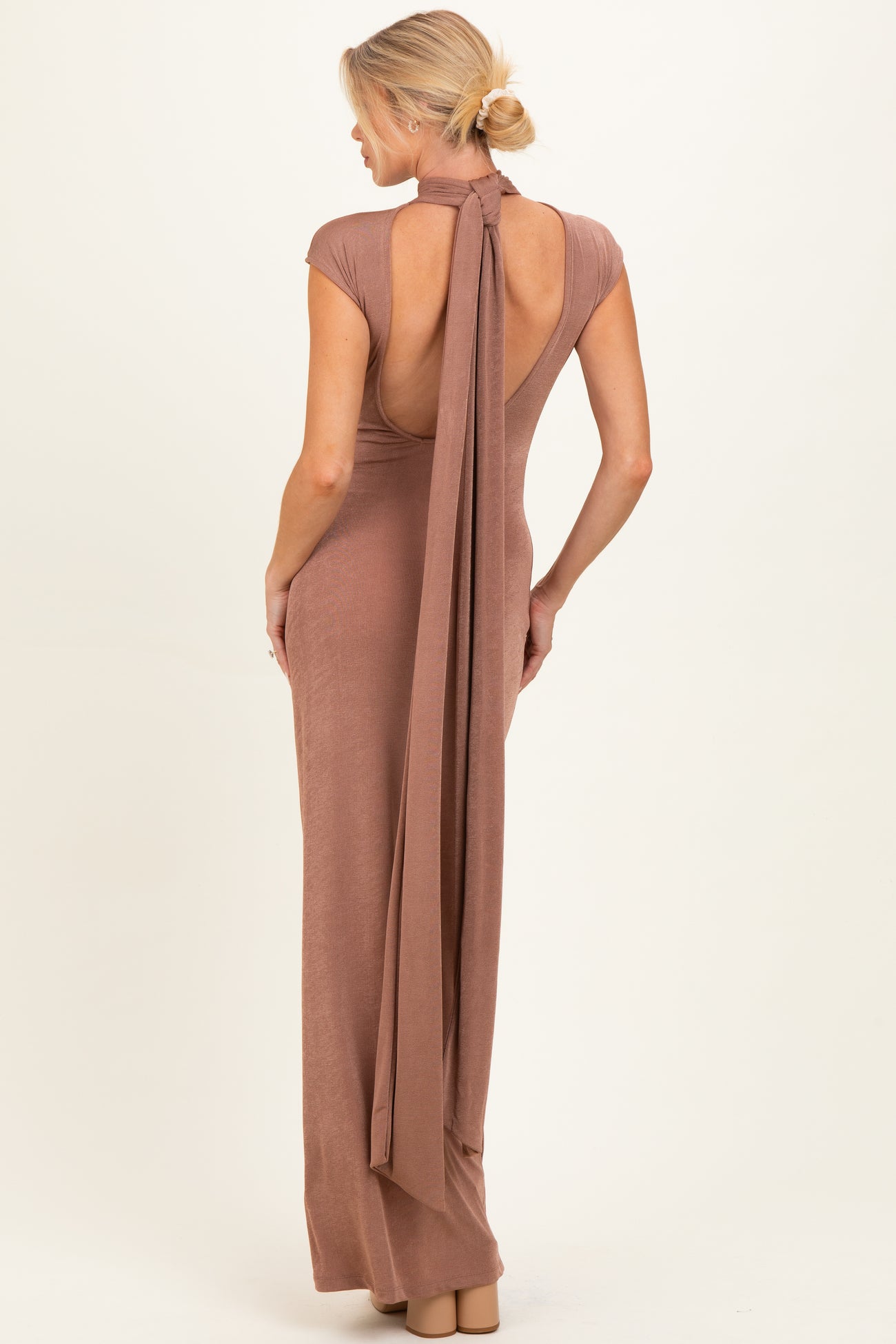 woman wearing a backless dusty rose maternity gown with a long tie detail at the neck