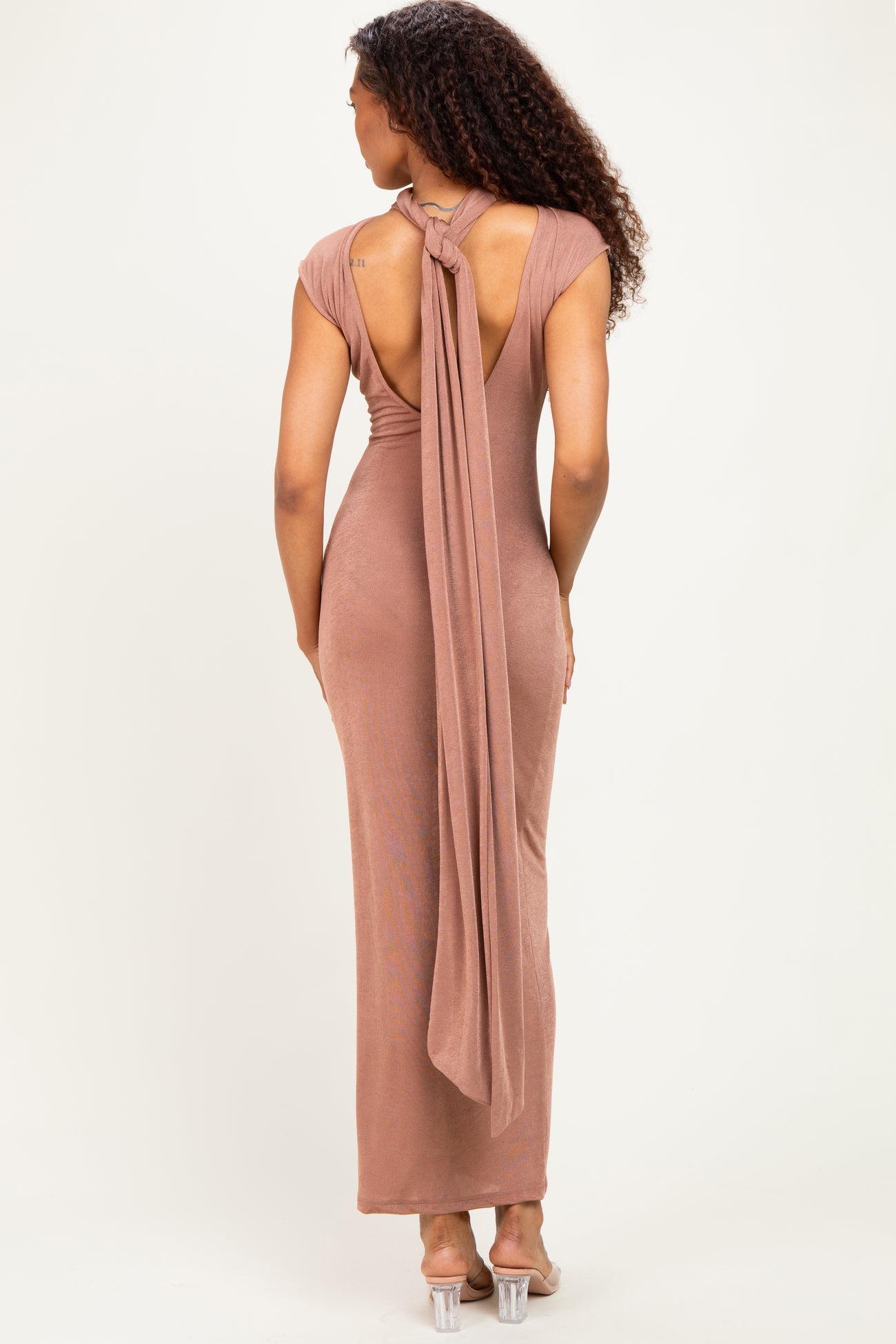 woman wearing a rose gold backless maxi dress with a tie detail at the neck and a fitted silhouette