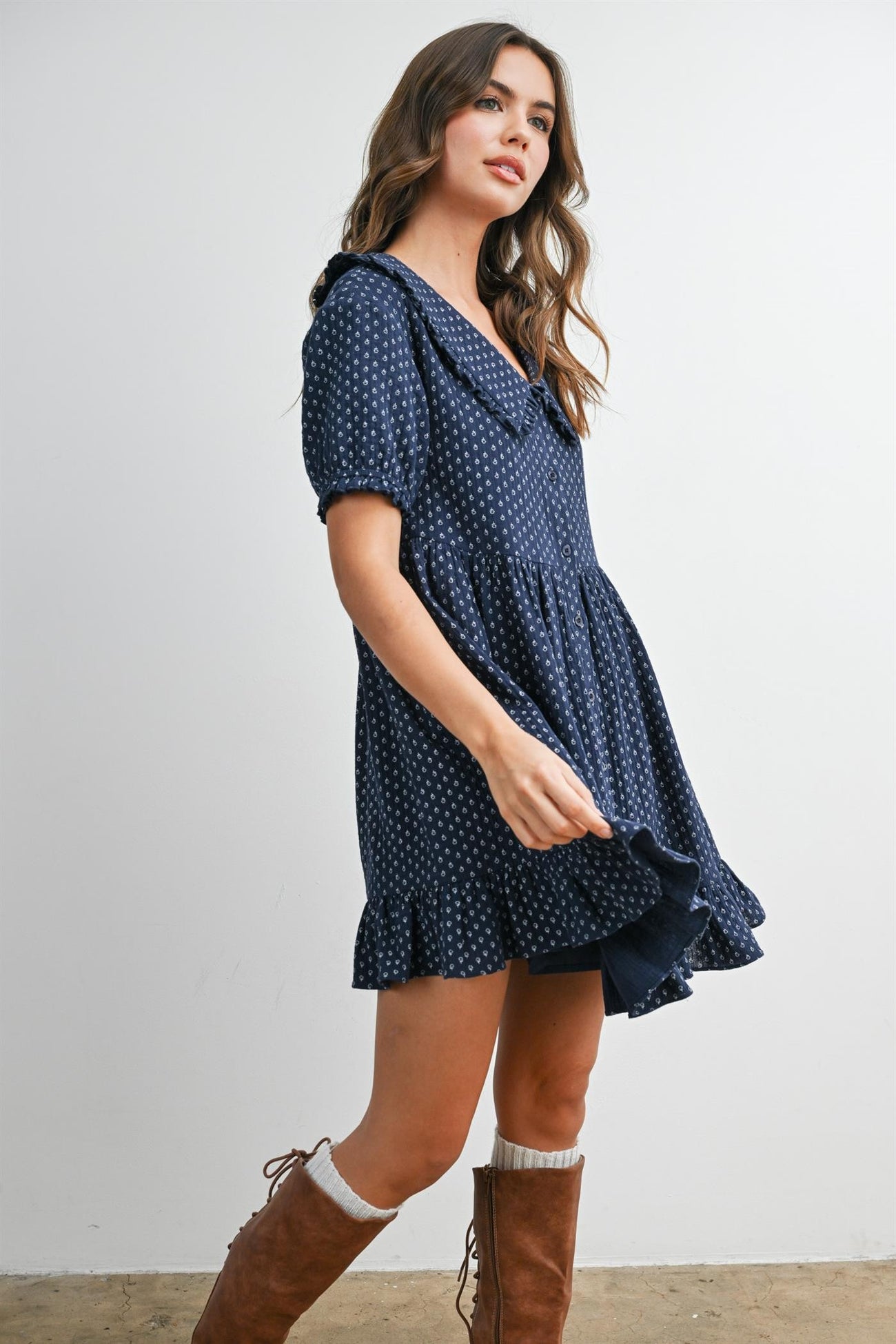 woman wearing a navy blue short sleeve dress with white polka dots and ruffled hem, paired with tan knee-high boots