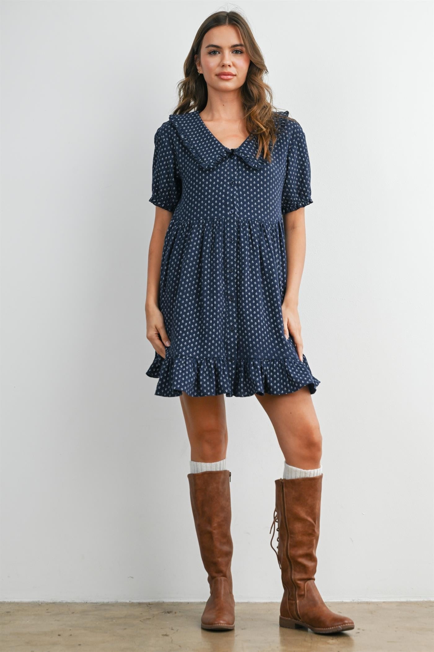 woman wearing a navy polka dot dress with a collar and ruffled hem, paired with tall brown boots