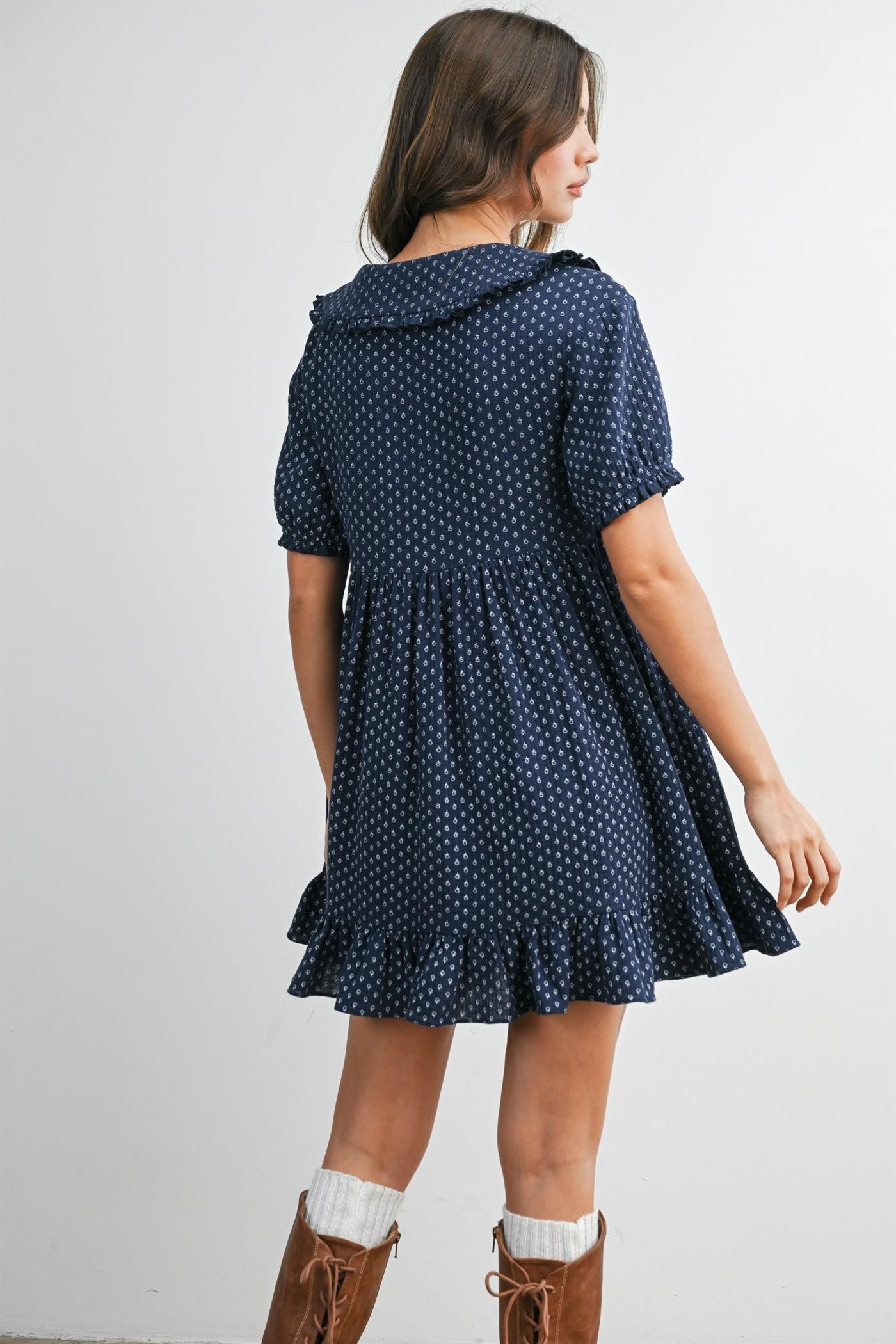woman wearing a navy blue short sleeve dress with white polka dots and a ruffled hem, showing a back view