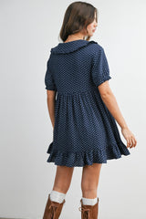 woman wearing a navy blue short sleeve dress with white polka dots and a ruffled hem, showing a back view