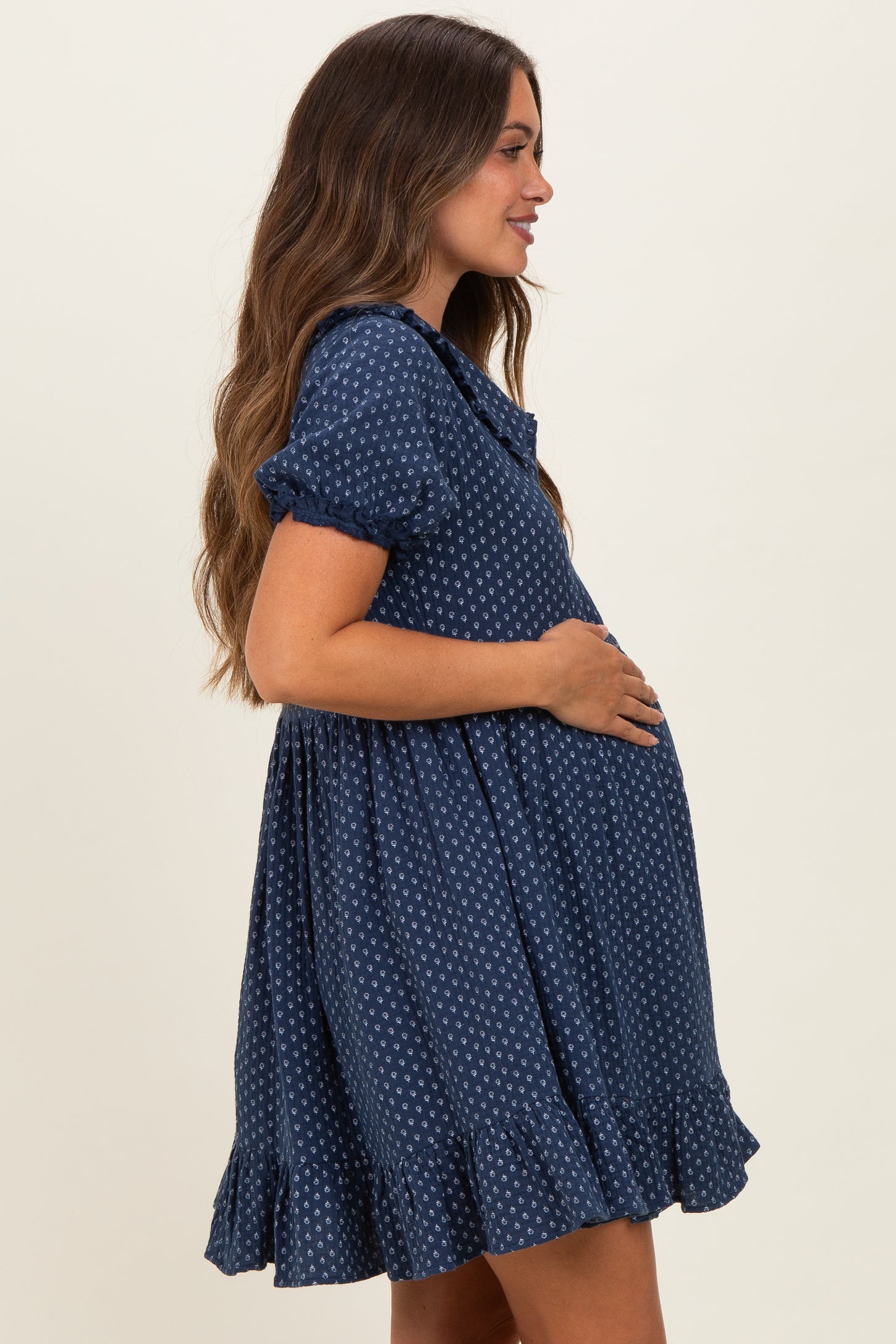 woman wearing a navy blue polka dot maternity dress with short sleeves and ruffled hem, showcasing her baby bump