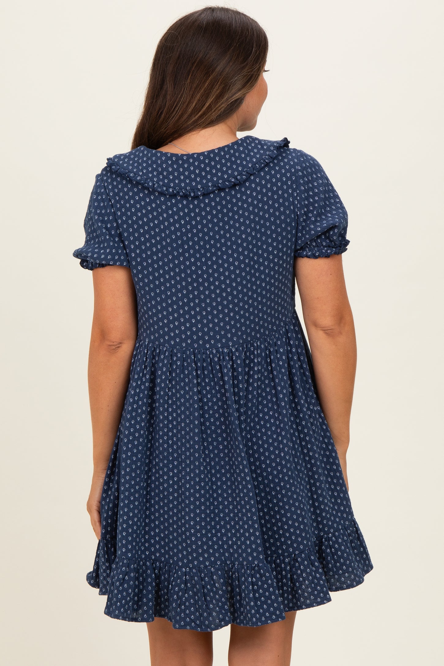 woman wearing a navy blue short sleeve maternity dress with a ruffled collar and a flared skirt