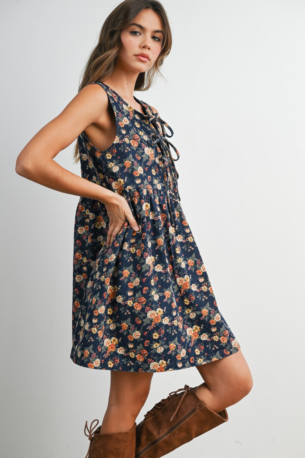 woman wearing a sleeveless navy floral print dress with a tie-front detail and pockets, paired with brown knee-high boots