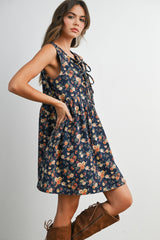 woman wearing a sleeveless navy floral print dress with a tie-front detail and pockets, paired with brown knee-high boots