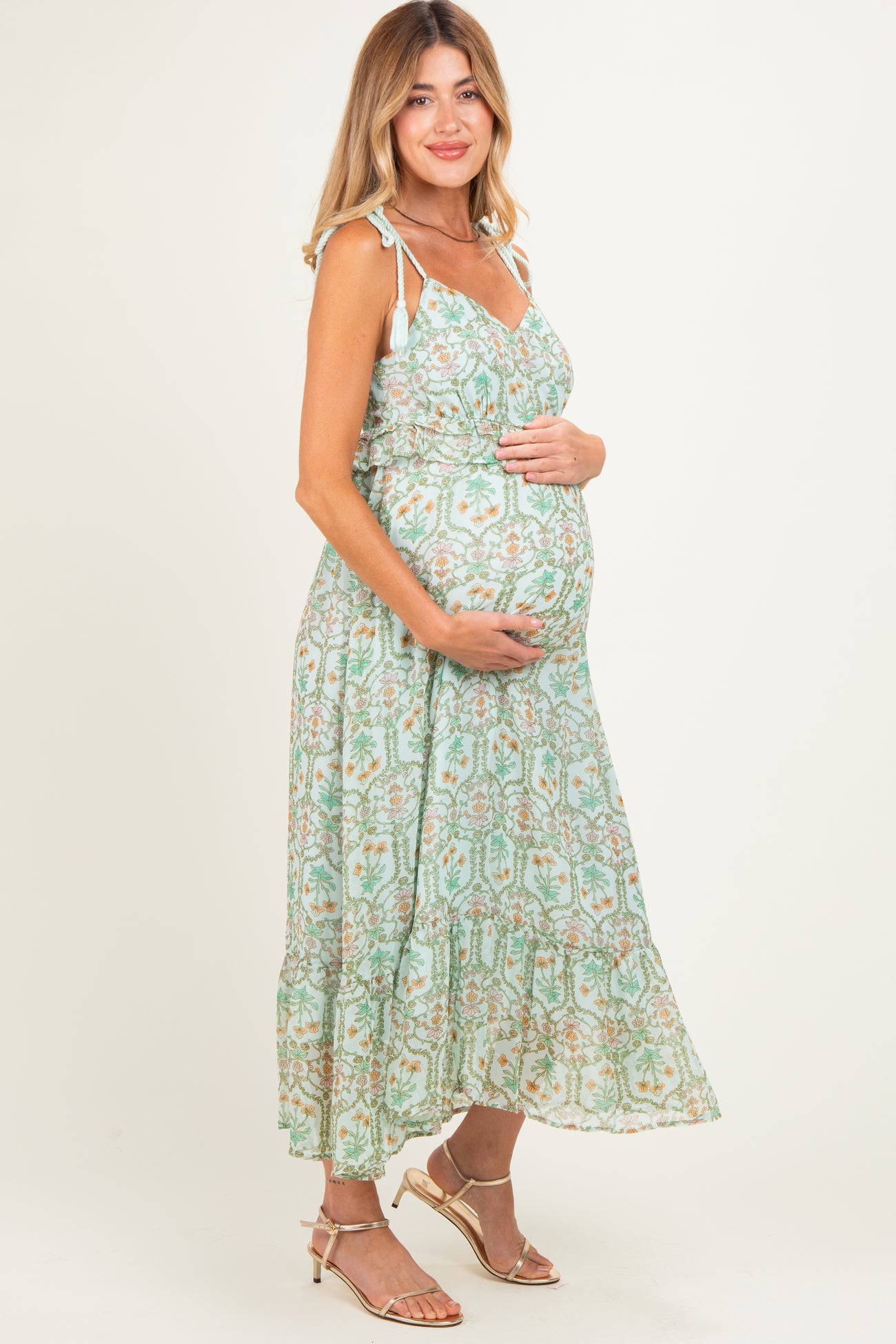 woman wearing a light green floral maternity maxi dress and cradling her baby bump