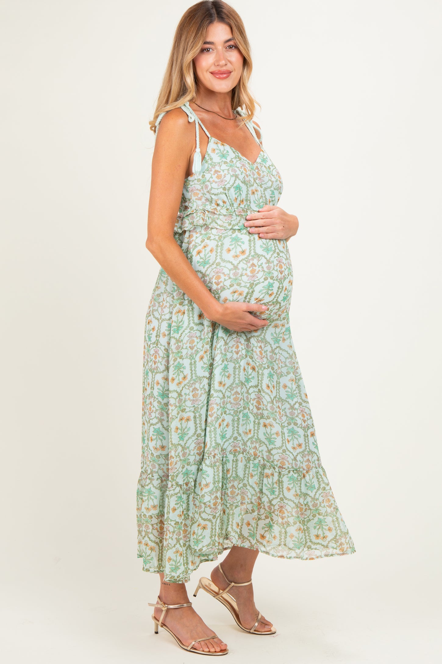 woman wearing a light green floral maternity maxi dress and cradling her baby bump