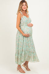 woman wearing a light green floral maternity maxi dress and cradling her baby bump