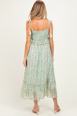 woman wearing a mint green maternity maxi dress with floral print and tie shoulder straps, showing a baby bump