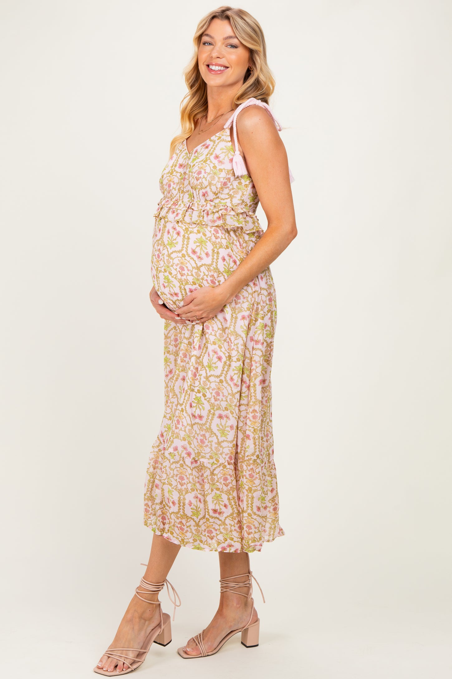 woman wearing a pink floral maternity maxi dress with ruffle details and a visible baby bump