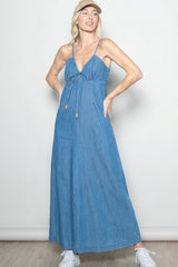 woman wearing a light blue maxi dress with spaghetti straps and a front tie detail, styled with a cap and white sneakers