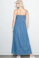 woman wearing a back view of a denim maxi dress with smocked bodice and straps, paired with a beige cap