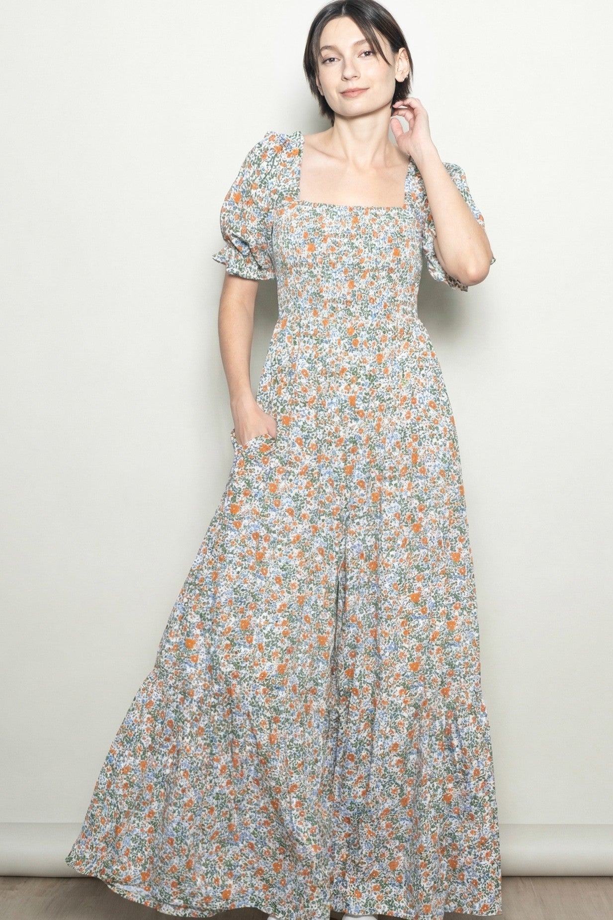 woman wearing a floral maxi dress with puff sleeves and pockets, standing against a light background