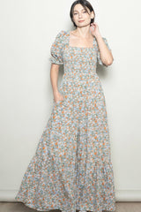 woman wearing a floral maxi dress with puff sleeves and pockets, standing against a light background