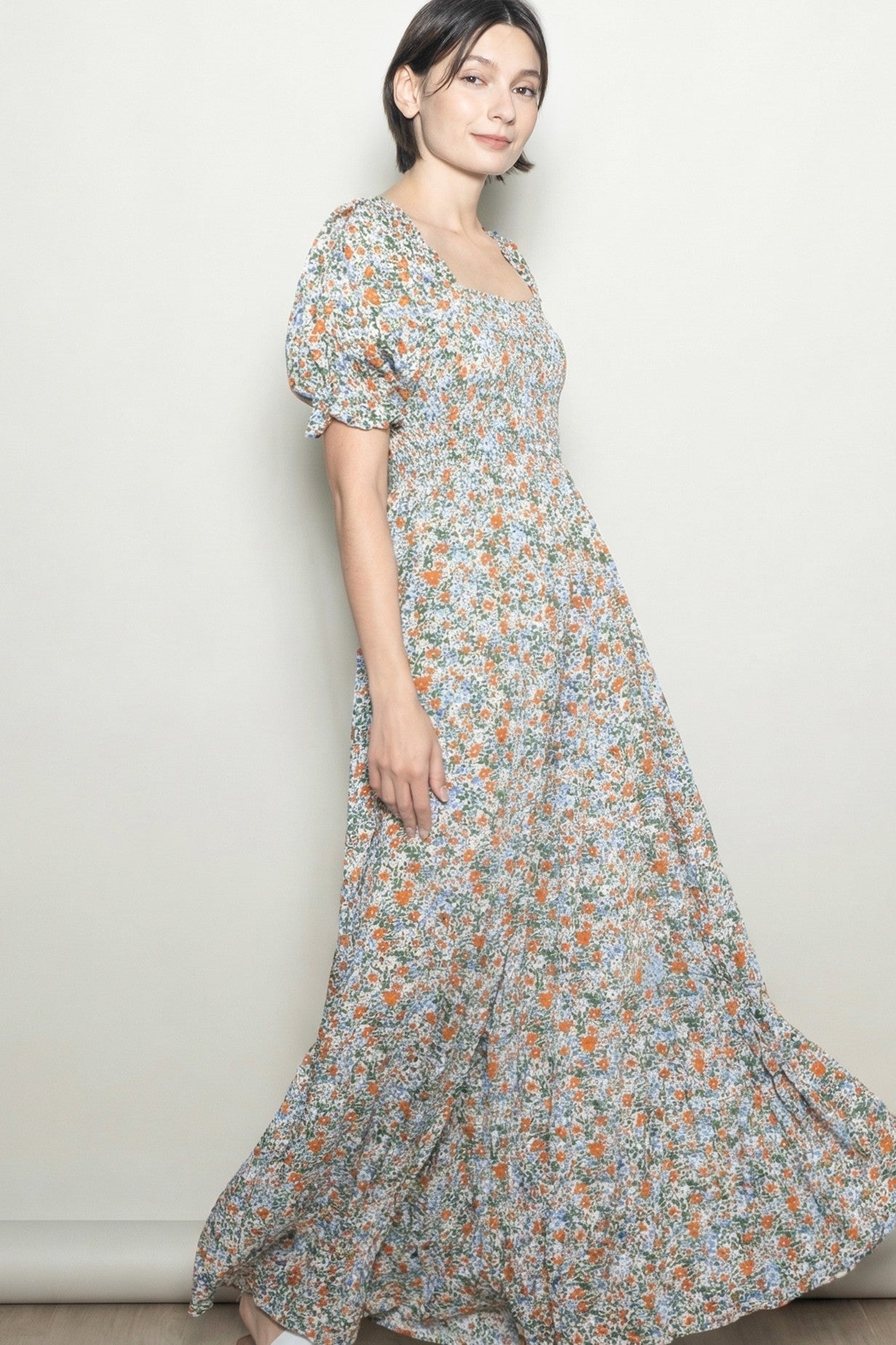 woman wearing a floral maxi dress with puff sleeves and a square neckline in a light pastel color scheme