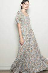 woman wearing a floral maxi dress with puff sleeves and a square neckline in a light pastel color scheme