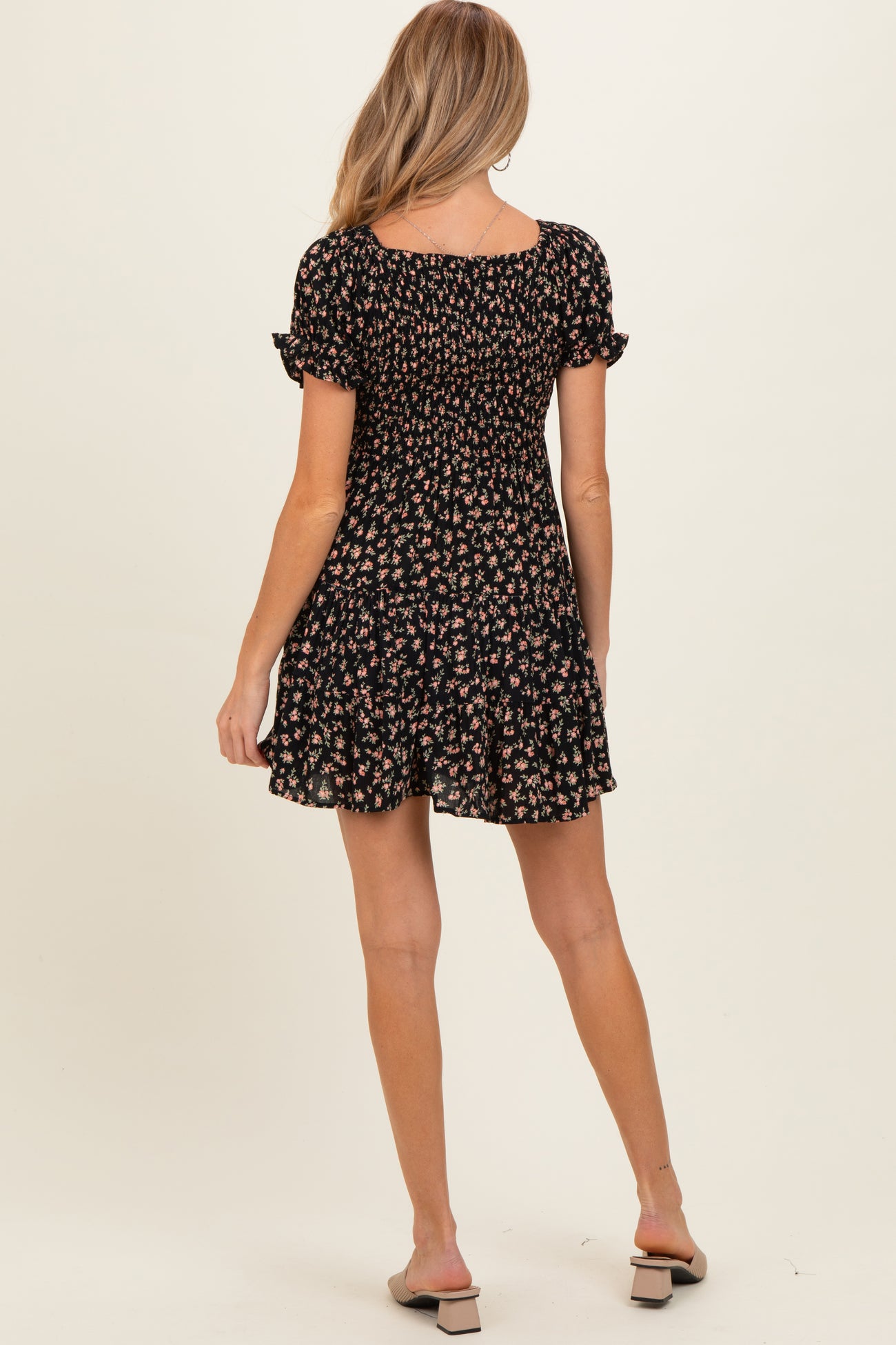 woman wearing a black floral maternity dress with short sleeves and a ruffled hem, facing away from the camera