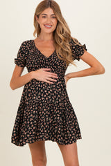 woman wearing a black floral maternity dress with short sleeves, smiling and holding her baby bump
