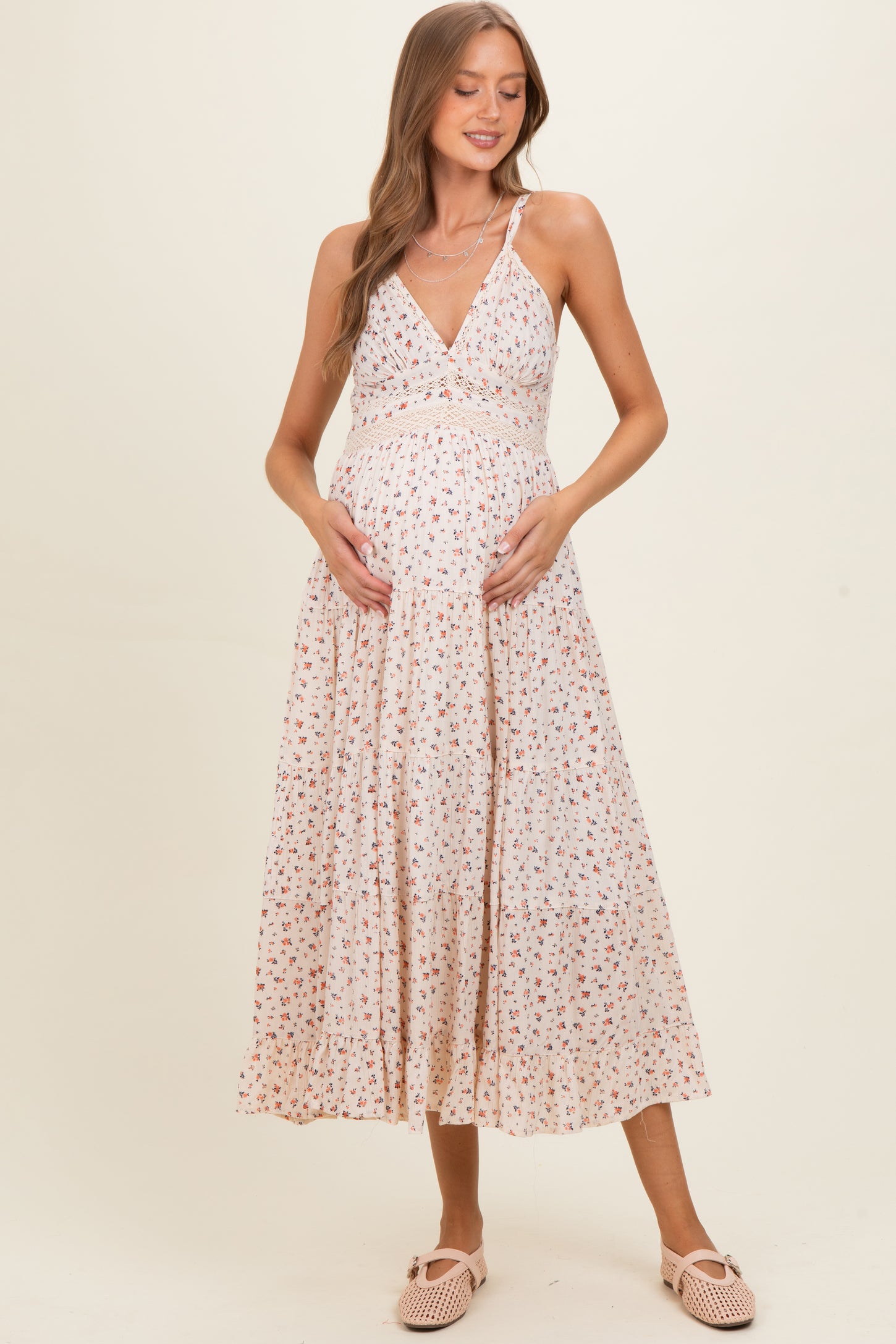 woman wearing a floral print maternity dress with a fitted bodice and flowy skirt, cradling her baby bump