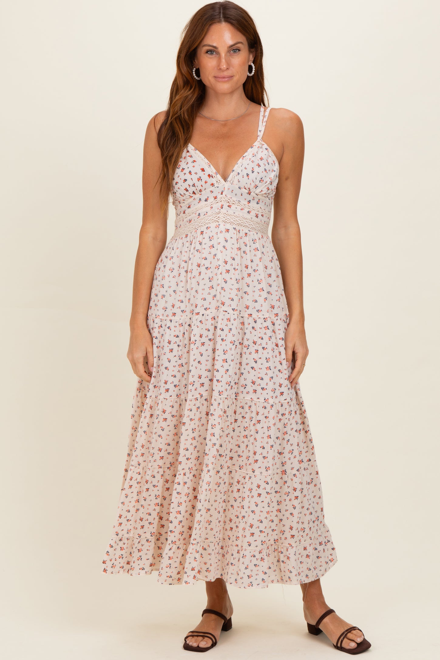 woman wearing a floral print maxi dress with spaghetti straps and a fitted bodice, standing on a neutral background