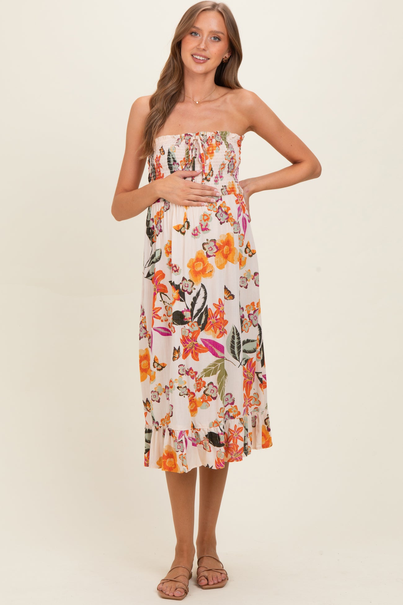 woman wearing a strapless floral maternity dress, showing her baby bump and standing in a relaxed pose