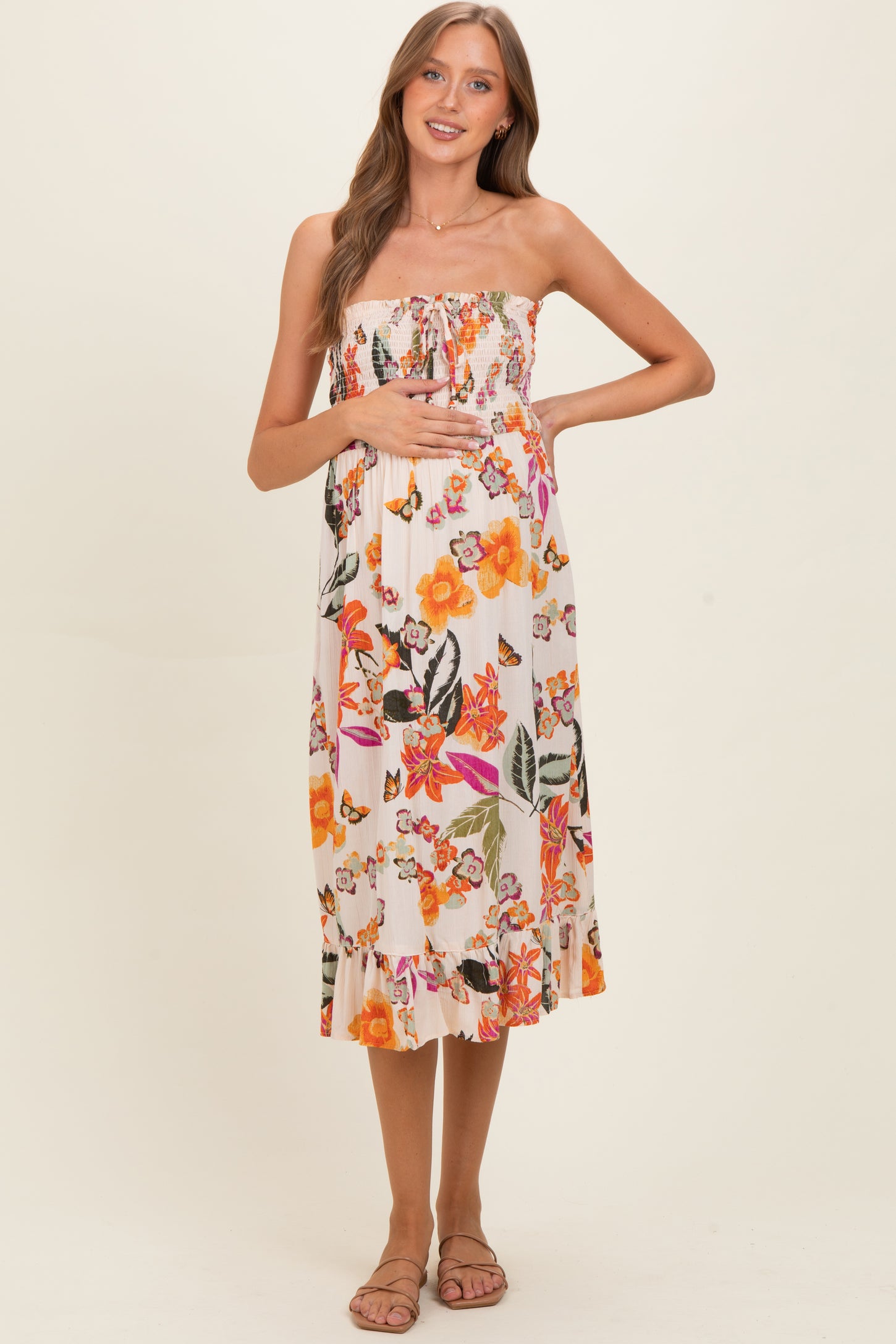 woman wearing a strapless floral maternity dress, showing her baby bump and standing in a relaxed pose