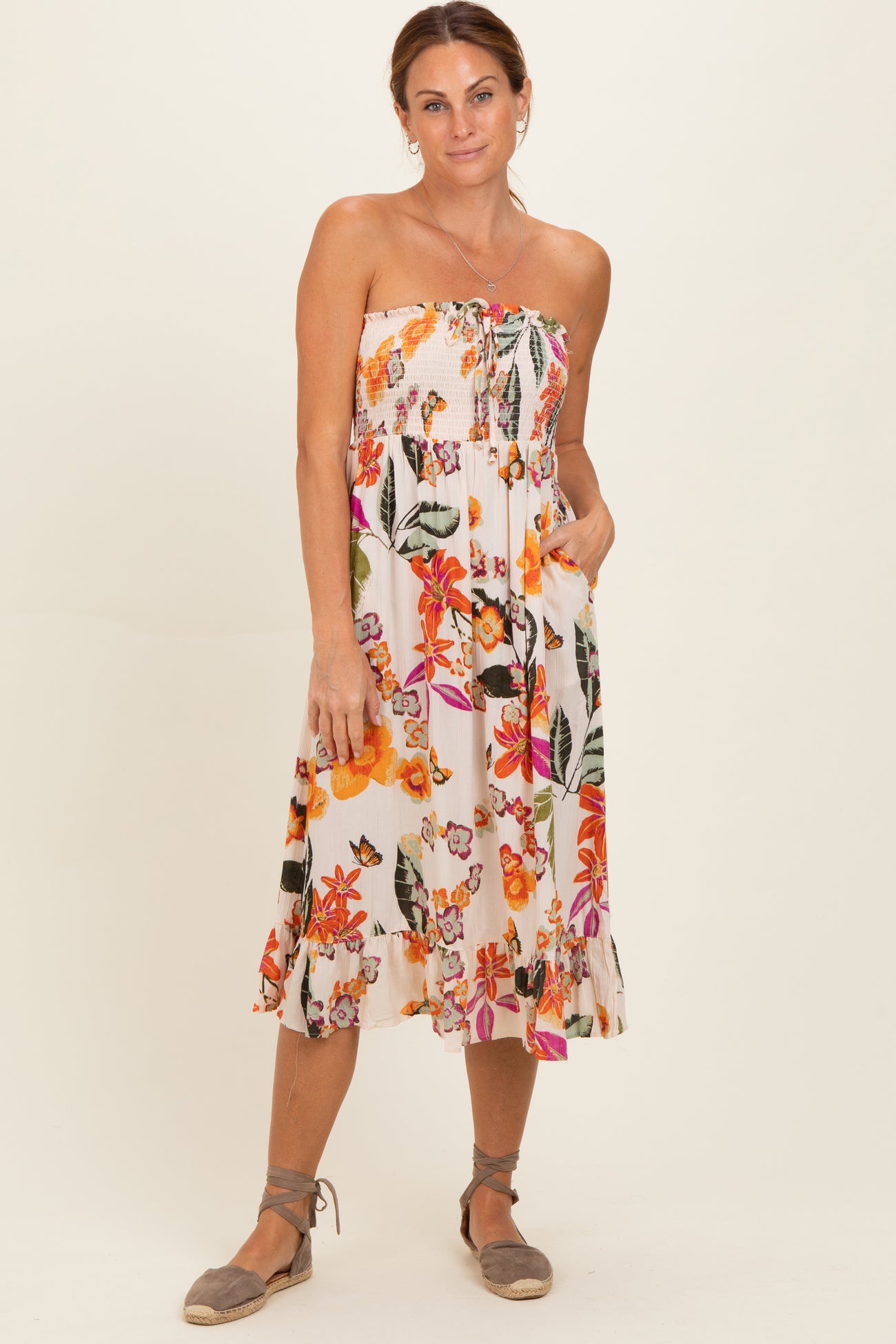 woman wearing a strapless floral midi dress with a smocked bodice and side pockets, standing with a relaxed pose