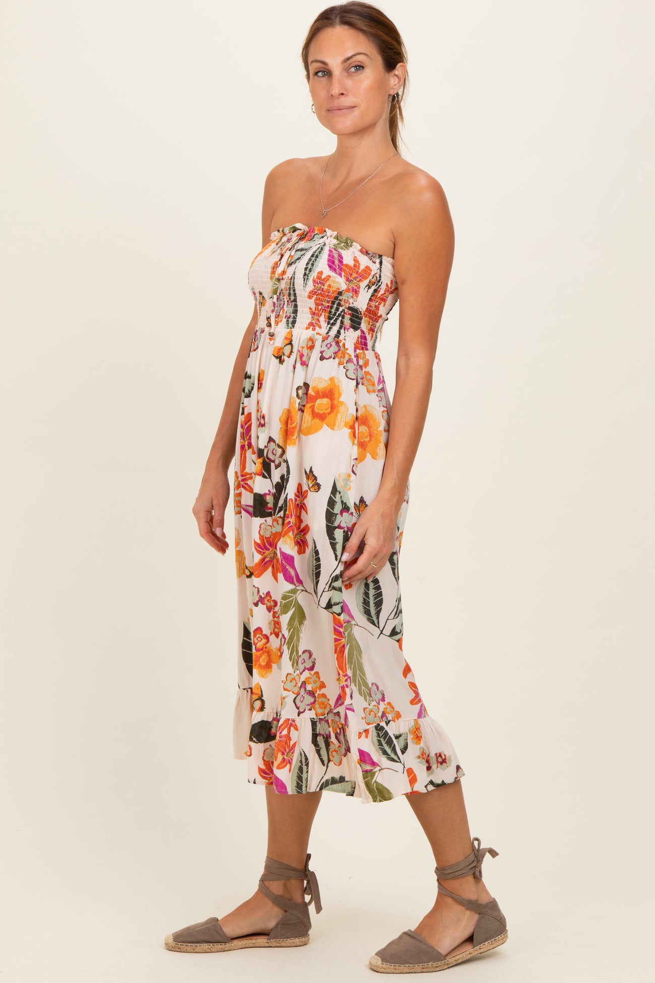 woman wearing a strapless floral midi dress with orange and pink flowers, standing and looking to the side