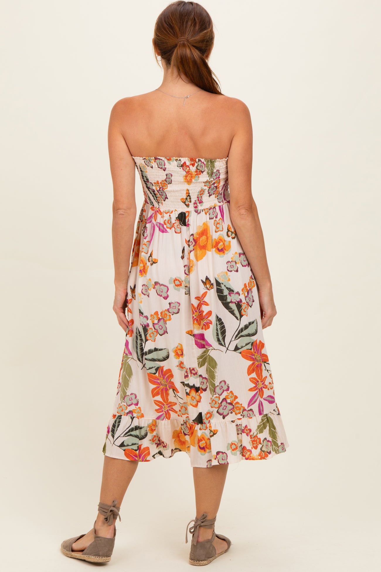 woman wearing a floral strapless midi dress with a smocked bodice and a flared hem, seen from the back
