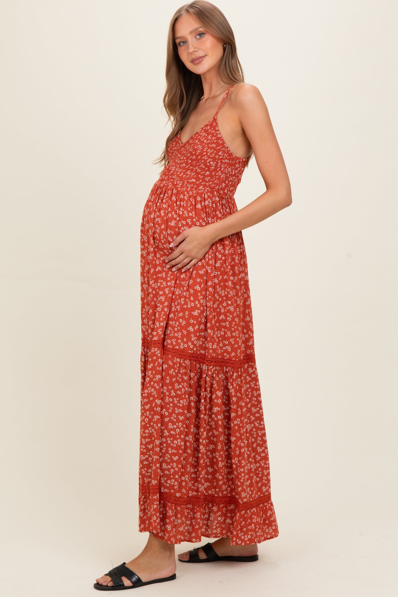 woman wearing a red floral maternity maxi dress and gently holding her baby bump
