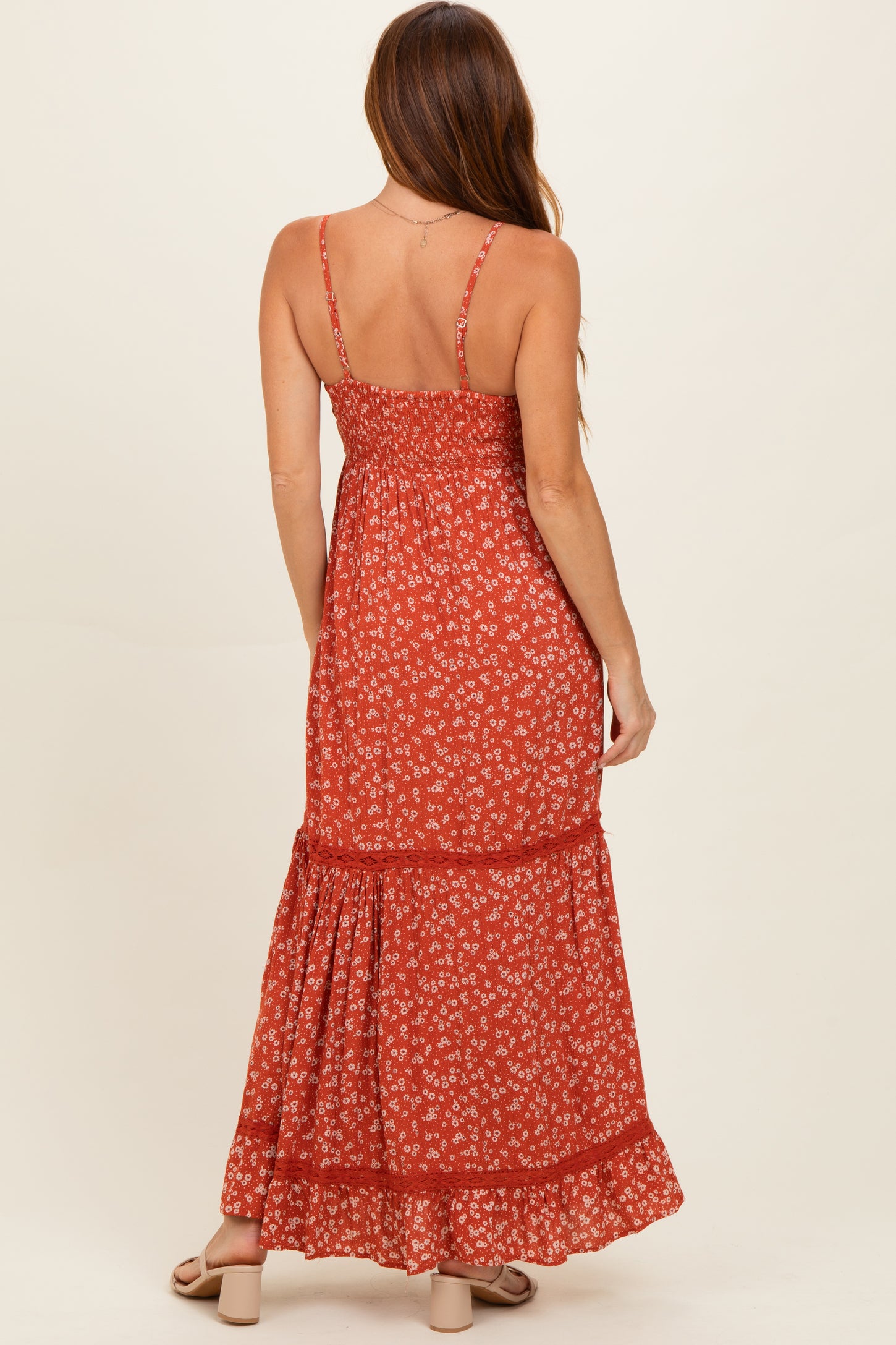 woman wearing a rust floral maxi dress with spaghetti straps and a tiered skirt, view from the back