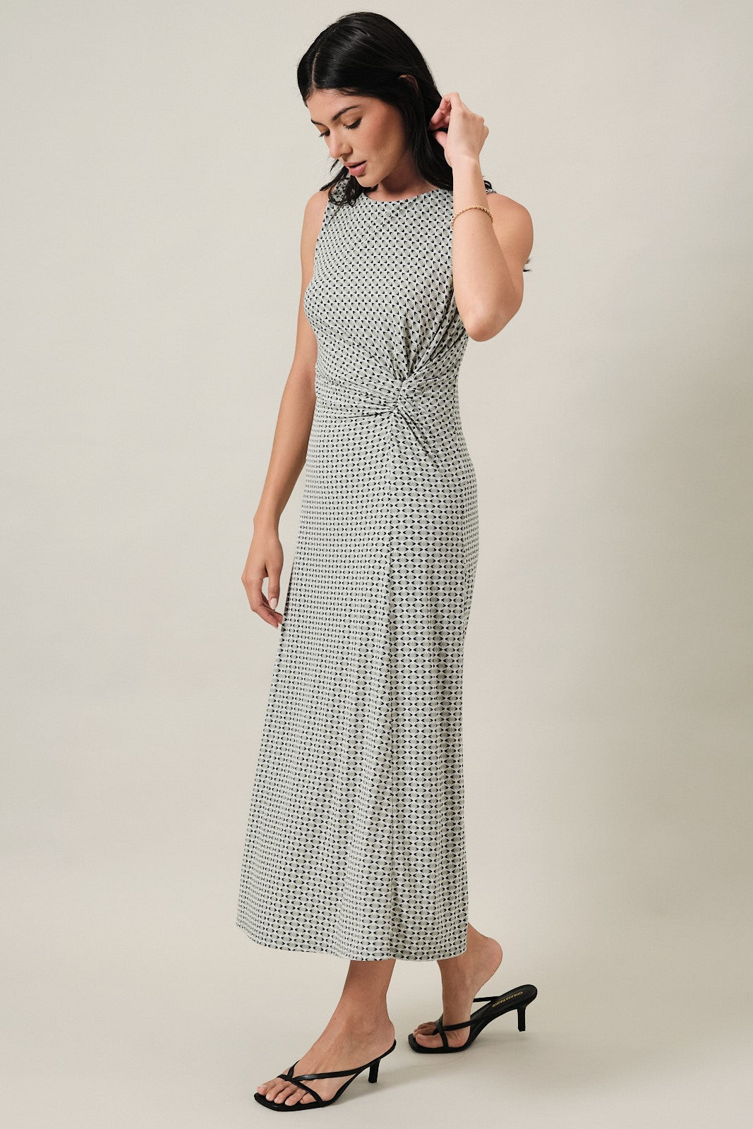 woman wearing a sleeveless black and white patterned midi dress with a knotted waist and side slit
