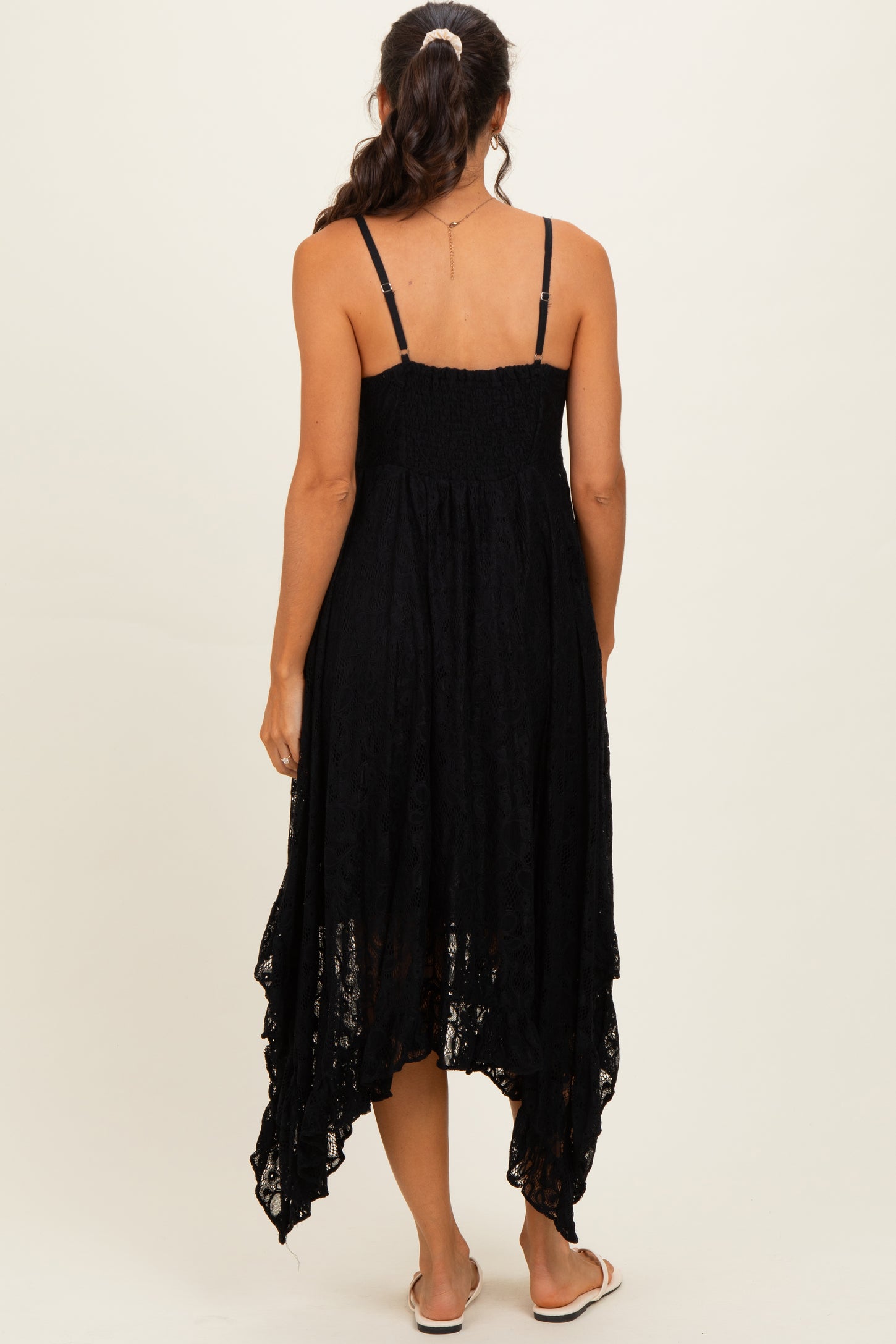 woman wearing a black lace high-low sundress with thin straps and a smocked bodice, seen from the back