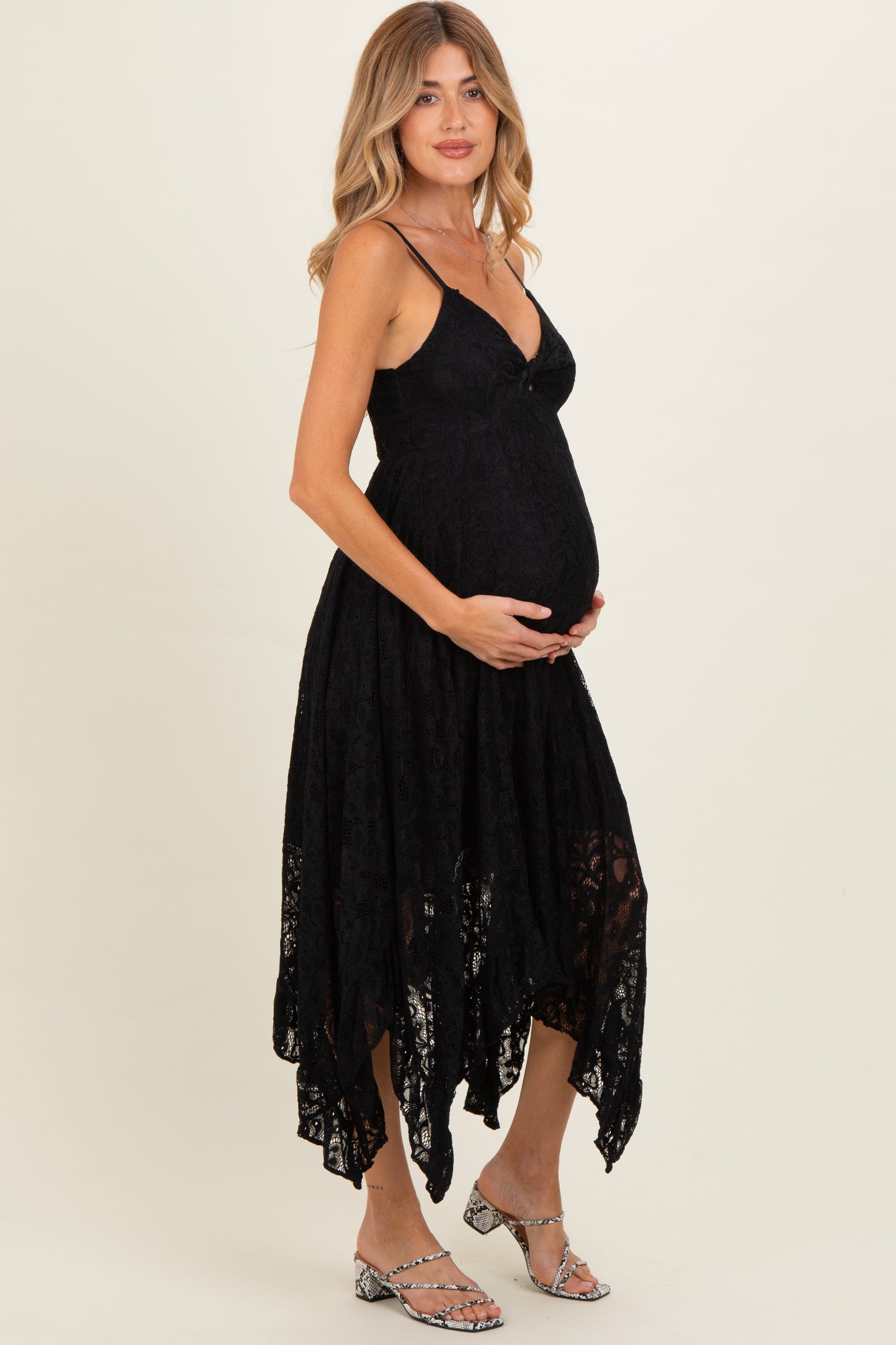 woman wearing a black lace maternity dress with an asymmetrical hemline and holding her baby bump