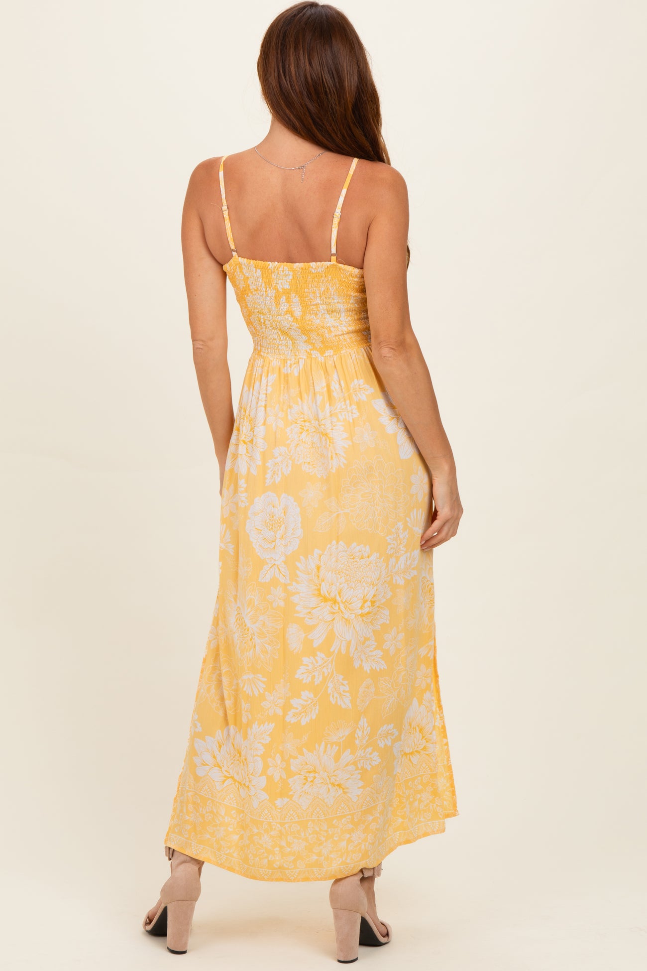 woman wearing a yellow floral maxi dress with a smocked bodice and thin straps, showing the back view