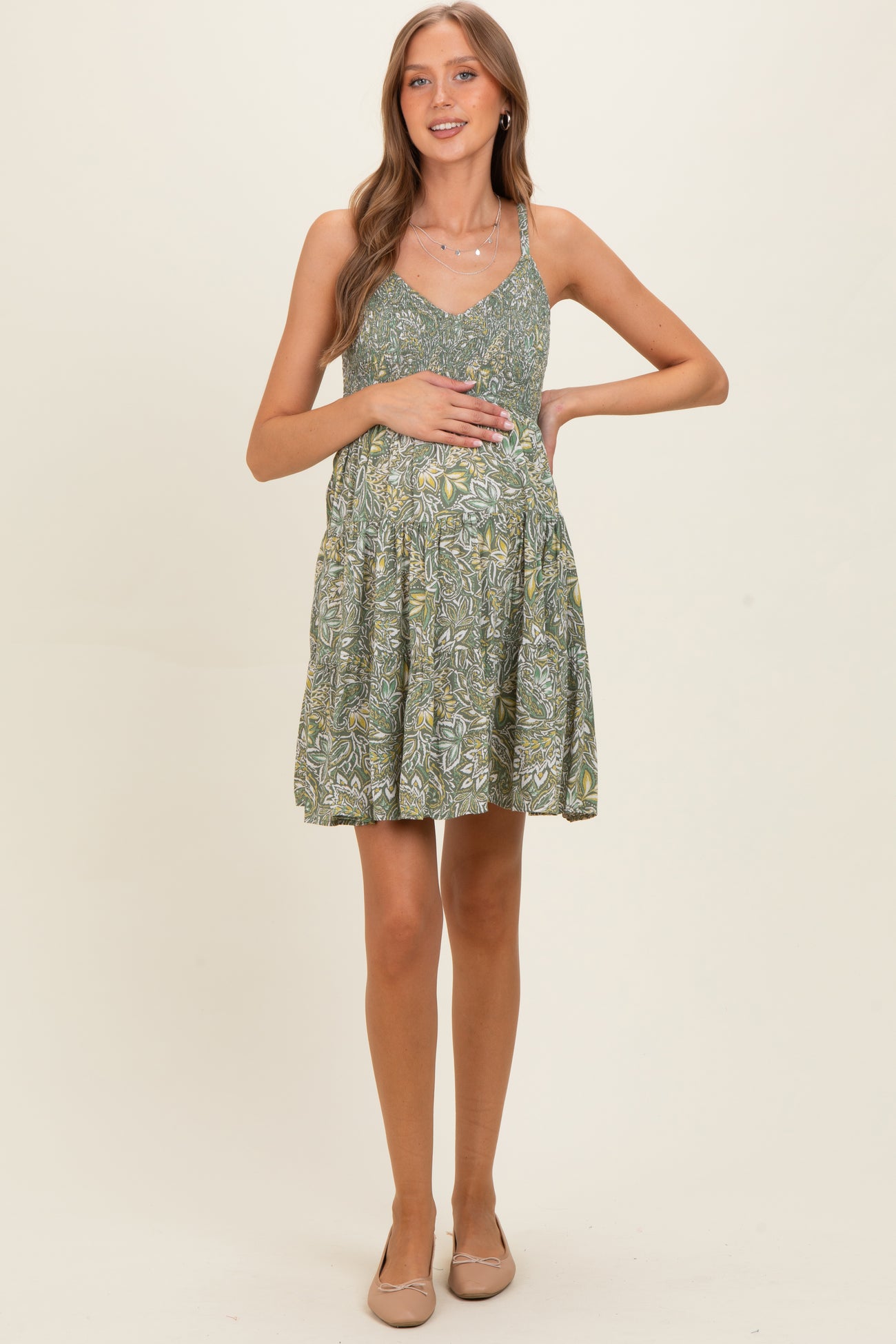 woman wearing a green floral maternity dress and holding her baby bump