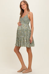 woman wearing a green floral maternity dress with a fitted bodice and flared skirt, showing her baby bump